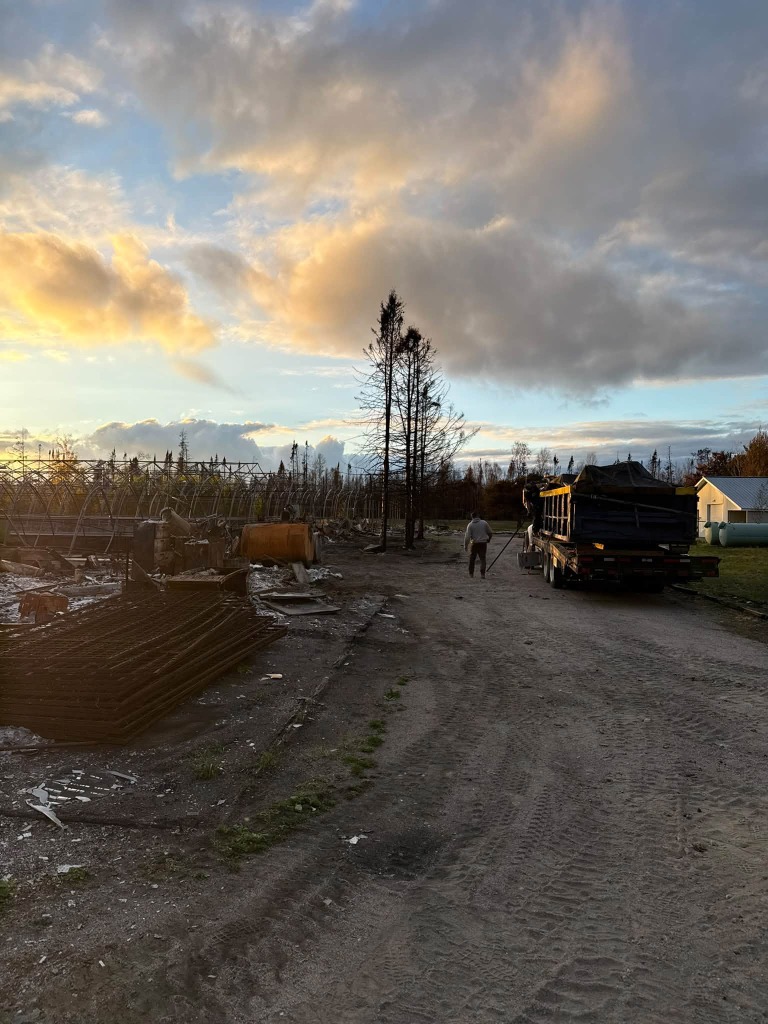 Debris haul truck and roll-off bin trailer removing fire rubble at sunset in Northwestern Ontario