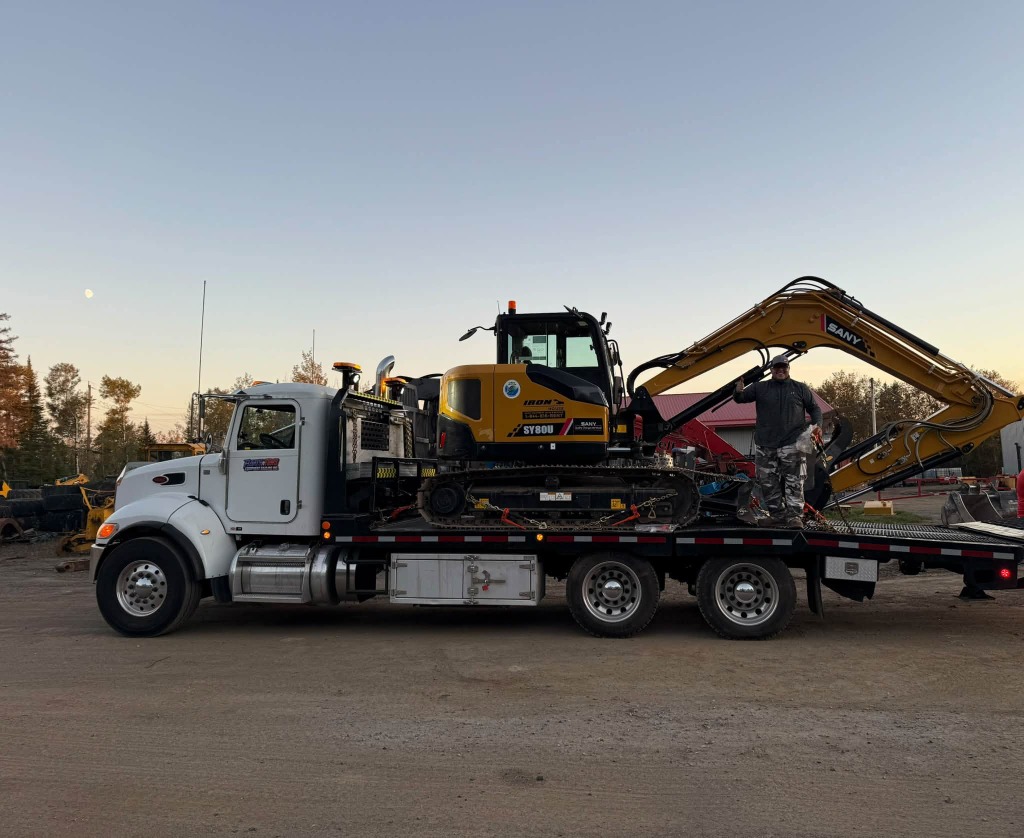 Heavy equipment float truck transporting yellow SANY excavator to wildfire rebuild zone in Northwestern Ontario